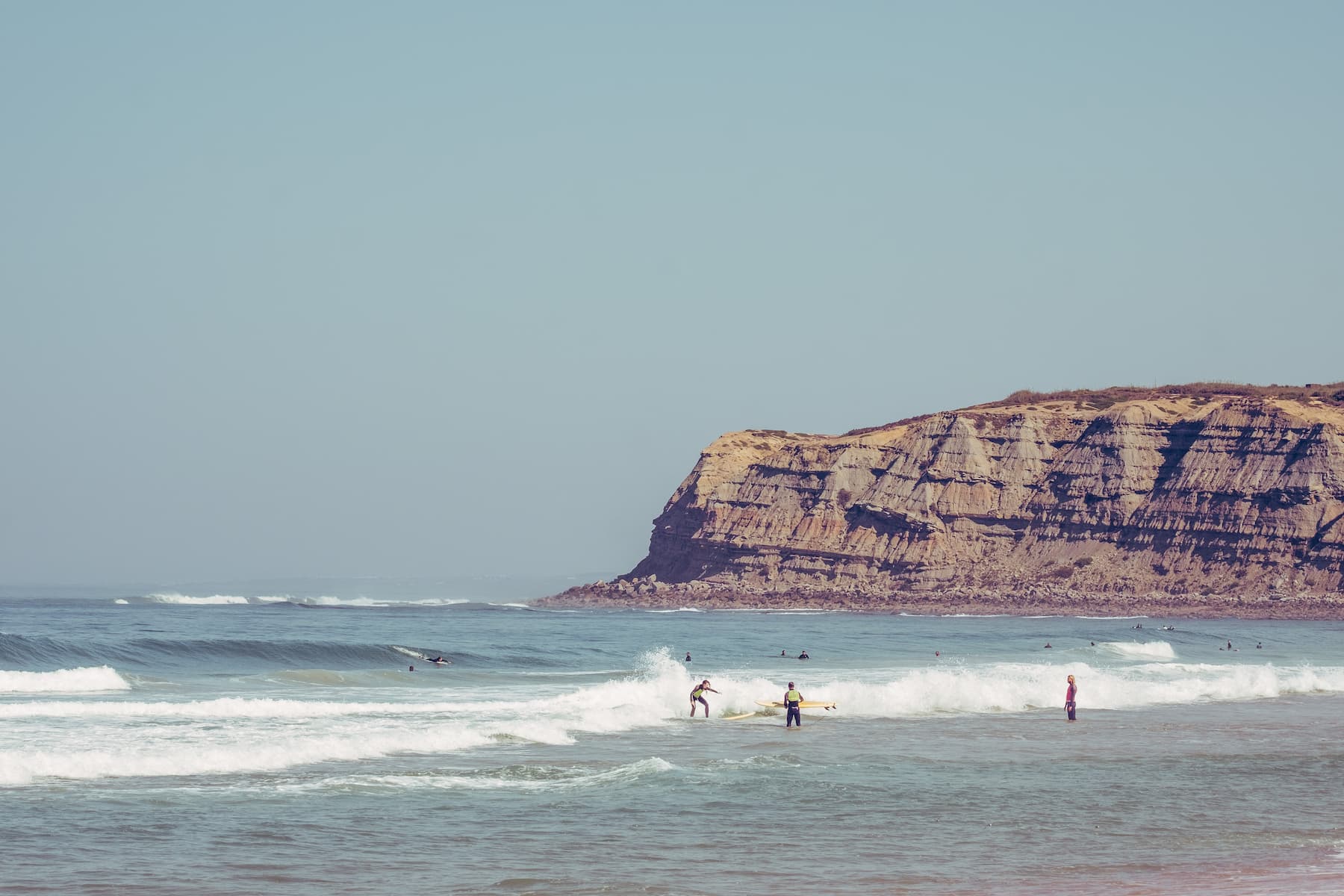 Surfschüler im Surfkurs mit Surflehrer und Klippen im Hintergrund